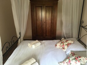 Un dormitorio con un armario de madera, una cama con ropa de cama blanca y almohadas estampadas con motivos florales.