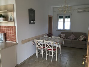 Una sala de estar acogedora con sofá, una mesa de comedor con sillas, una araña y una ventana con persianas.