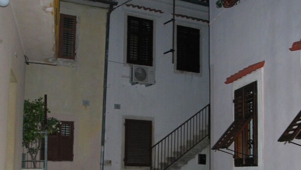 Une ruelle étroite pavée de pierres, bordée de bâtiments blancs, avec un escalier et des plantes en pot.
