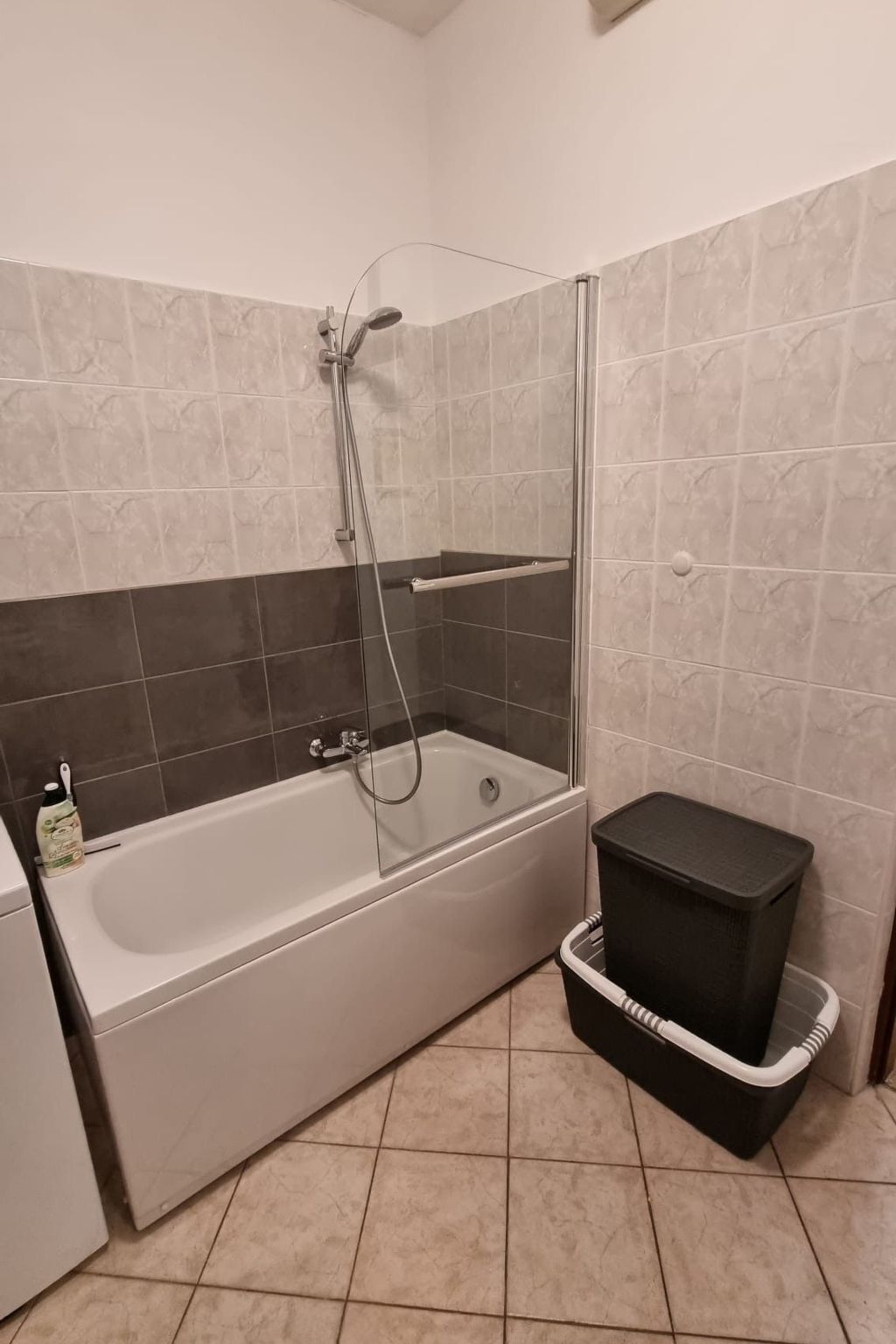 A bathroom with a bathtub, shower, and a black trash bin.
