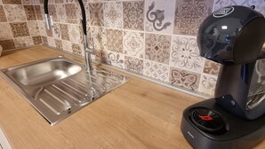 Une cuisine dotée d’un évier en acier inoxydable, d’une machine à café noire et d’un dosseret carrelé aux motifs variés.