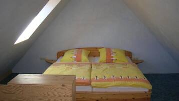 Ein kleines, gemütliches Schlafzimmer im Dachgeschoss mit schrägen Wänden, einem hölzernen Bett mit gelber Bettwäsche und einem kleinen Holztisch.