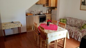 Et kompakt køkken med træskabe, et spisebord med stole og en sofa i en lille opholdsstue.