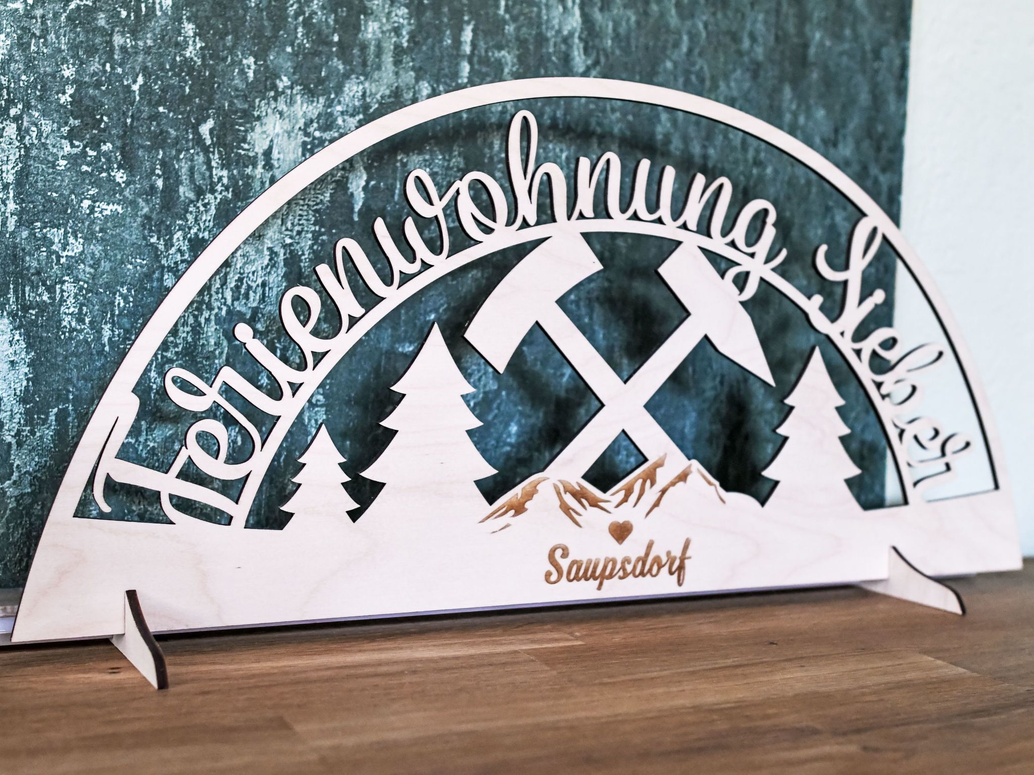 Un letrero de madera con el texto 'Treibenuwwohnung Sausdorf' y símbolos de montaña y cruz.