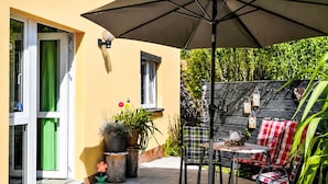An outdoor patio with a table and chairs, a large umbrella, potted plants, and a wooden fence. - Siebers by Interhome (Altendorf)