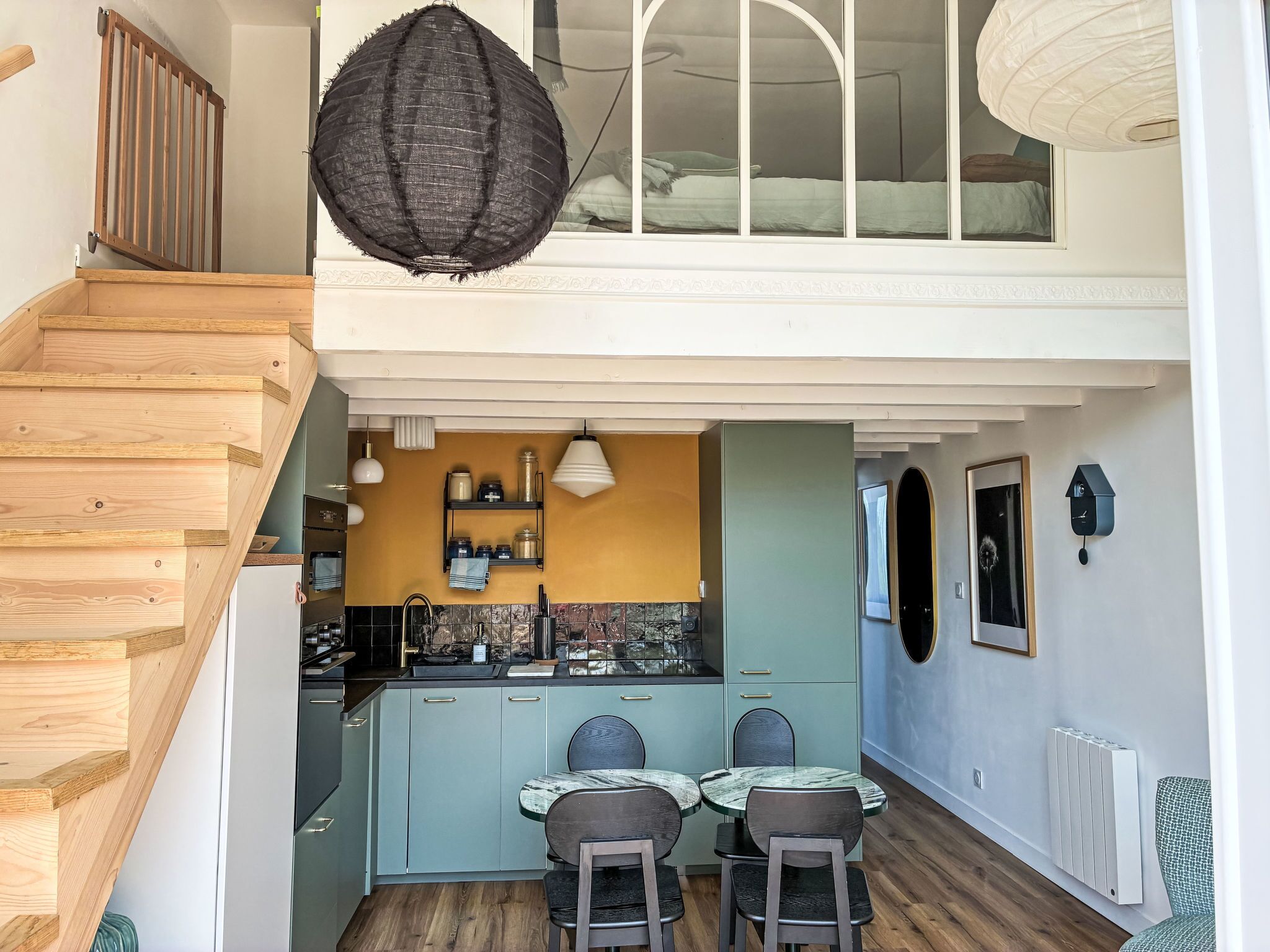 A modern kitchen with a dining area, wooden staircase, and a loft bedroom with a view.