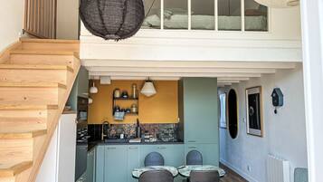 A modern kitchen with a dining area, wooden staircase, and a loft bedroom with a view.