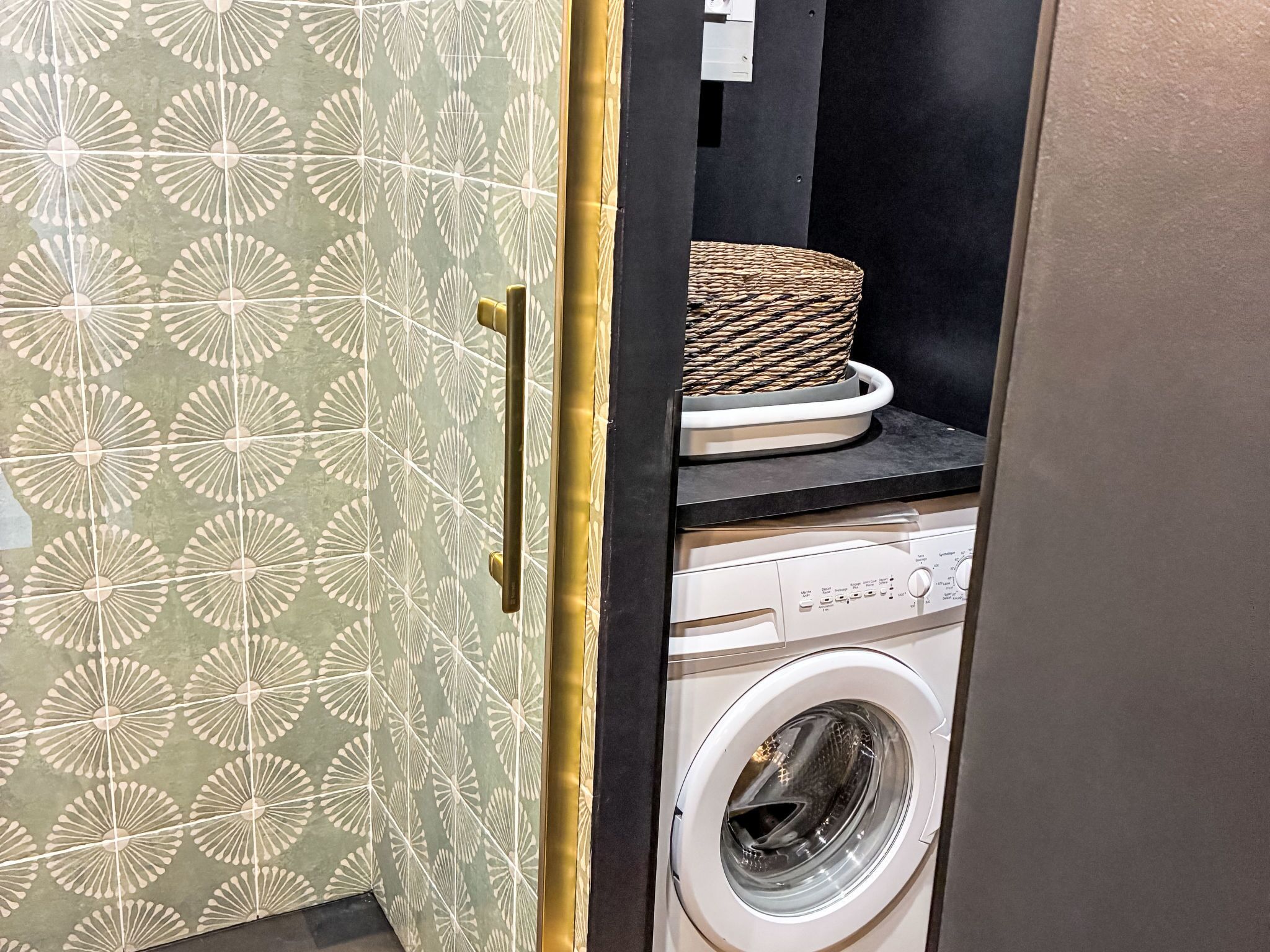Een wasmachine met een bedieningspaneel, een mand bovenop en decoratieve kastdeuren.