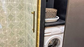 Een wasmachine met een bedieningspaneel, een mand bovenop en decoratieve kastdeuren.