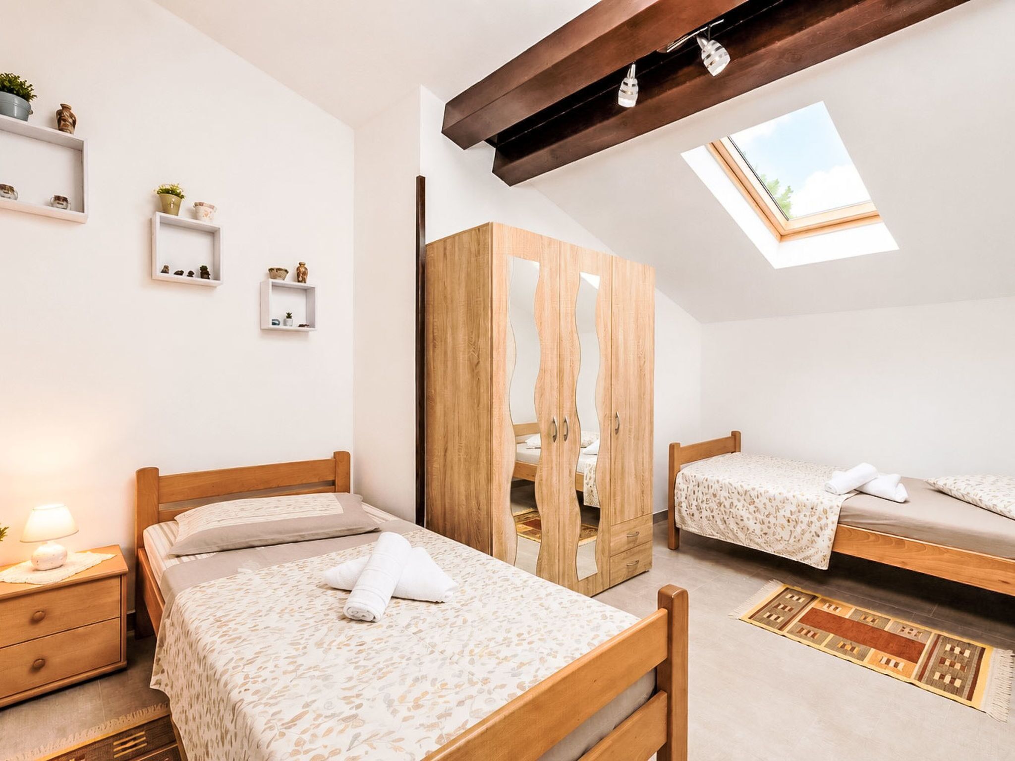 A bedroom with two beds, a wardrobe, a skylight, and bedside tables with lamps.