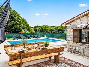 A poolside area with a wooden bench, lounge chairs, and a stone building with a window. - Haus Plum by Interhome (Drenje)