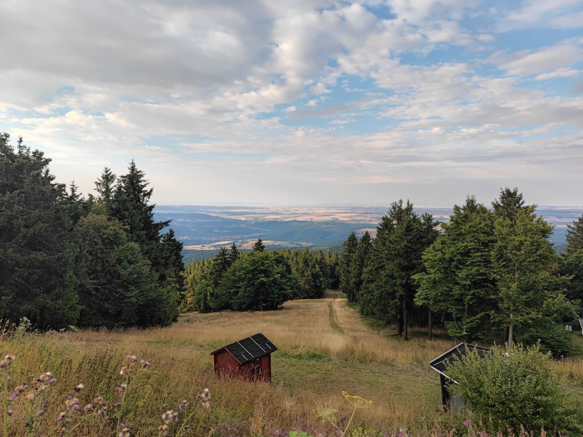 Un paysage rural caractérisé par un ciel dégagé, un chemin de terre et deux petites constructions en bois.