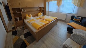 Une chambre à coucher avec un lit en bois, un canapé, un miroir et une fenêtre avec des rideaux.