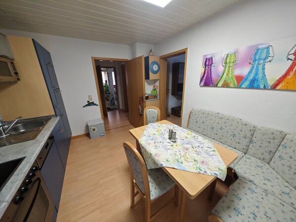 Cocina compacta con lavamanos, estufa y armarios, una mesa de comedor con sillas y un sofá.