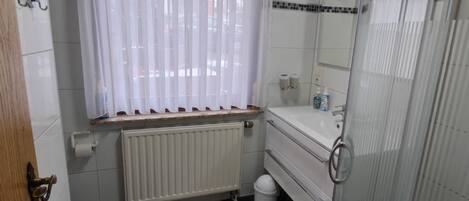 A bathroom with a toilet, a sink, a shower, and a radiator.