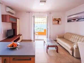 A living room with a sofa, a glass coffee table, a TV on a wooden cabinet, and a balcony with curtains. - Modernes Apartment mit zwei Schlafzimmern by Interhome (Rabac)