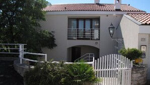 Un bâtiment à deux étages, doté d’un toit en tuiles, d’un balcon avec une rambarde en métal et d’une entrée fermée par un portail.