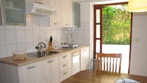 Une cuisine avec des meubles blancs, une table en bois et une vue sur la verdure à l’extérieur.