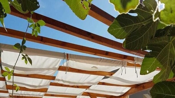 Un espacio exterior techado con piscina, pérgola de madera y sillones de descanso.