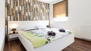 Un dormitorio moderno con una cama grande, una mesita de noche con lámpara, una obra de arte en la pared y una ventana con persianas.