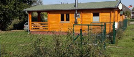 A wooden cabin with a green roof, a chimney, and a fenced area with a gate.