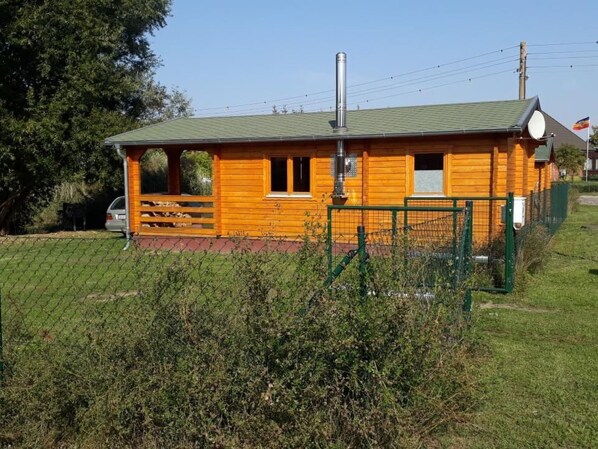 A wooden cabin with a green roof, a chimney, and a fenced area with a gate. - Blockhaus mit eigenem See by Interhome (Pasewalk)