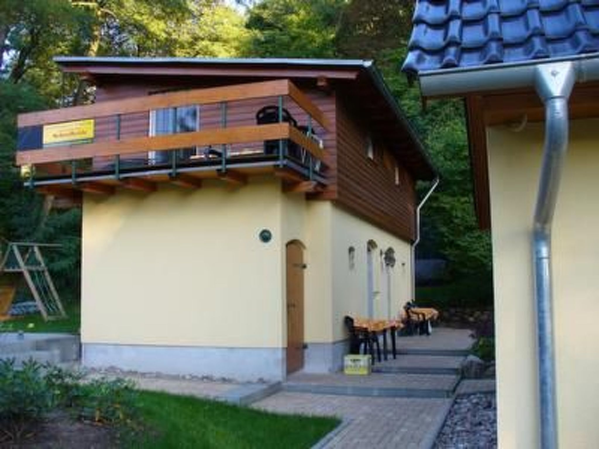 A building with a wooden upper floor and a lower beige wall, a metal staircase, and outdoor seating.
