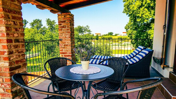 A covered patio with a round table and four chairs, a potted plant, and a view of a park and buildings in the background. - Istrien Haus neunte Pina by Interhome (Poreč/Kaštelir)
