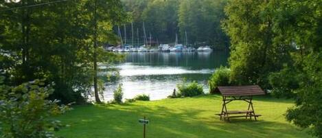 A grassy area with a wooden bench and a signpost, overlooking a lake with sailboats.