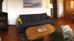 Ett vardagsrum med en soffa, ett soffbord i trä, en mönstrad pall, en tavla på väggen, en lampa och ett träskåp.