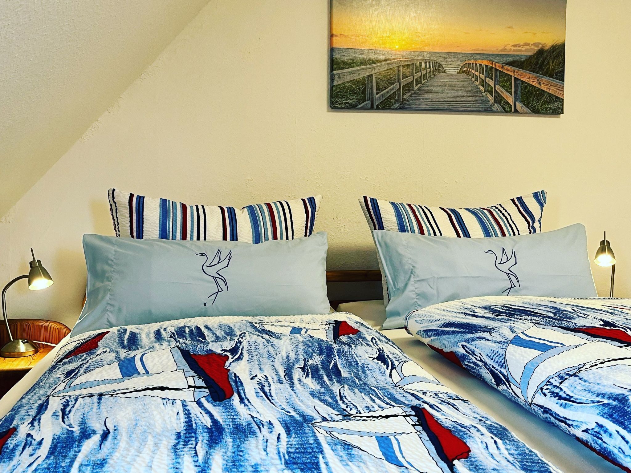 Ein Hotelzimmer mit zwei Betten, gestreiften Kissen und einem Gemälde, das einen Sonnenuntergang über einem Steg zeigt.