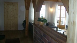 A wooden interior with a high ceiling, a wooden door, a seating area with a sofa and a table, and a window with curtains. - am Waldrand, ideal für Bergsport by Interhome (Oberstaufen)