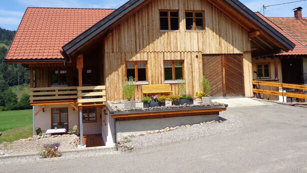 A wooden chalet with a sloped roof, a balcony, and a small porch area with seating. - am Waldrand, ideal für Bergsport by Interhome (Oberstaufen)