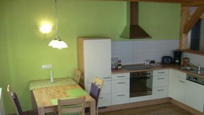 A compact kitchen with a wooden table and chairs, a stove, oven, and a sink. - am Waldrand, ideal für Bergsport by Interhome (Oberstaufen)