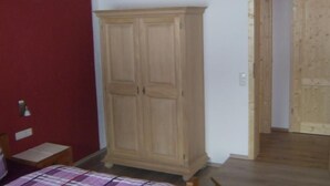 A bedroom with a wooden wardrobe, a bed with a plaid bedspread, and a red wall. - am Waldrand, ideal für Bergsport by Interhome (Oberstaufen)