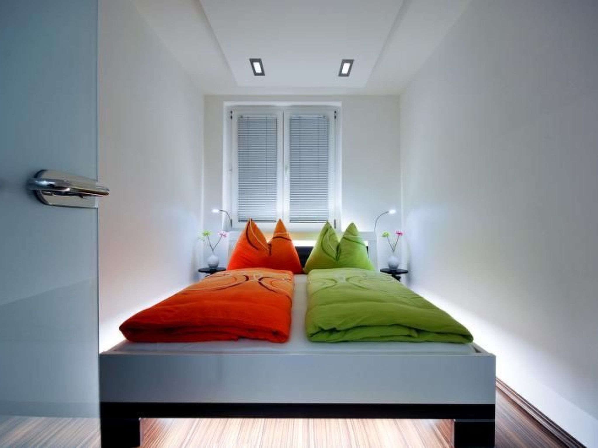 Un dormitorio moderno con cama, dos lámparas de noche y una ventana con persianas.