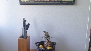 En inramad konstinstallation av Bremer Wind hänger ovanför ett träbord, och på bordet står en flätad korg fylld med frukt.