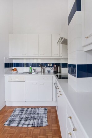 A modern kitchen with white cabinets, a blue and white backsplash, and a wooden floor. - Klimatisiertes 3 Zimmer Appartement  mit Terrasse by Interhome (Vienna)