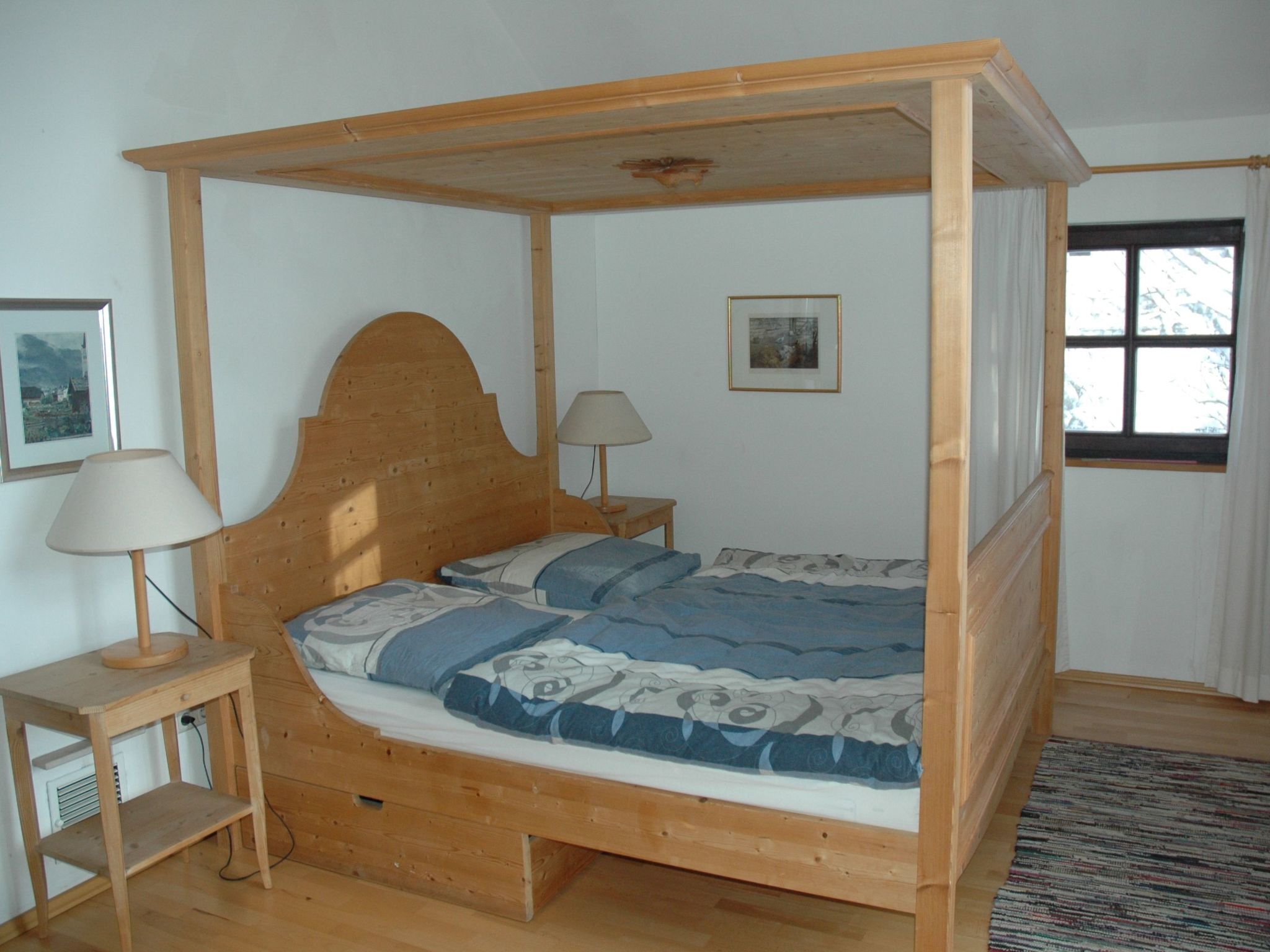 Un lit à baldaquin en bois, doté d’une tête de lit, de deux tables de chevet avec des lampes et d’une fenêtre avec des rideaux.