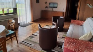 A living room with a wooden ceiling, a television on the wall, a sofa, a coffee table, and a dining area with chairs and a table. - Apartment Gaby by Interhome (Bonndorf)