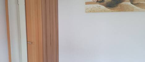 A room with a purple sofa, a wooden wardrobe, and a painting of flowers on the wall.