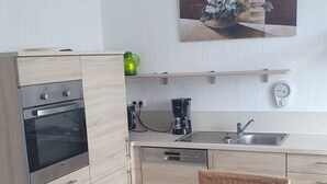 A modern kitchen with light wood cabinetry, a built-in oven, a coffee maker, and a sink.