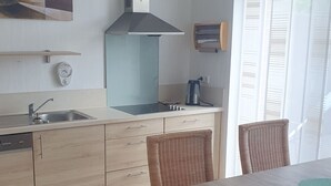 A modern kitchen with a wooden countertop, stainless steel sink, and a built-in stove. There is a wicker chair with a cushion and a dining table with a green placemat.