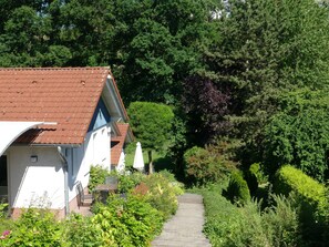 Ett hus med ett rött tegeltak, en vit fasad och en trädgård med en stenlagd gångväg som leder till entrén.