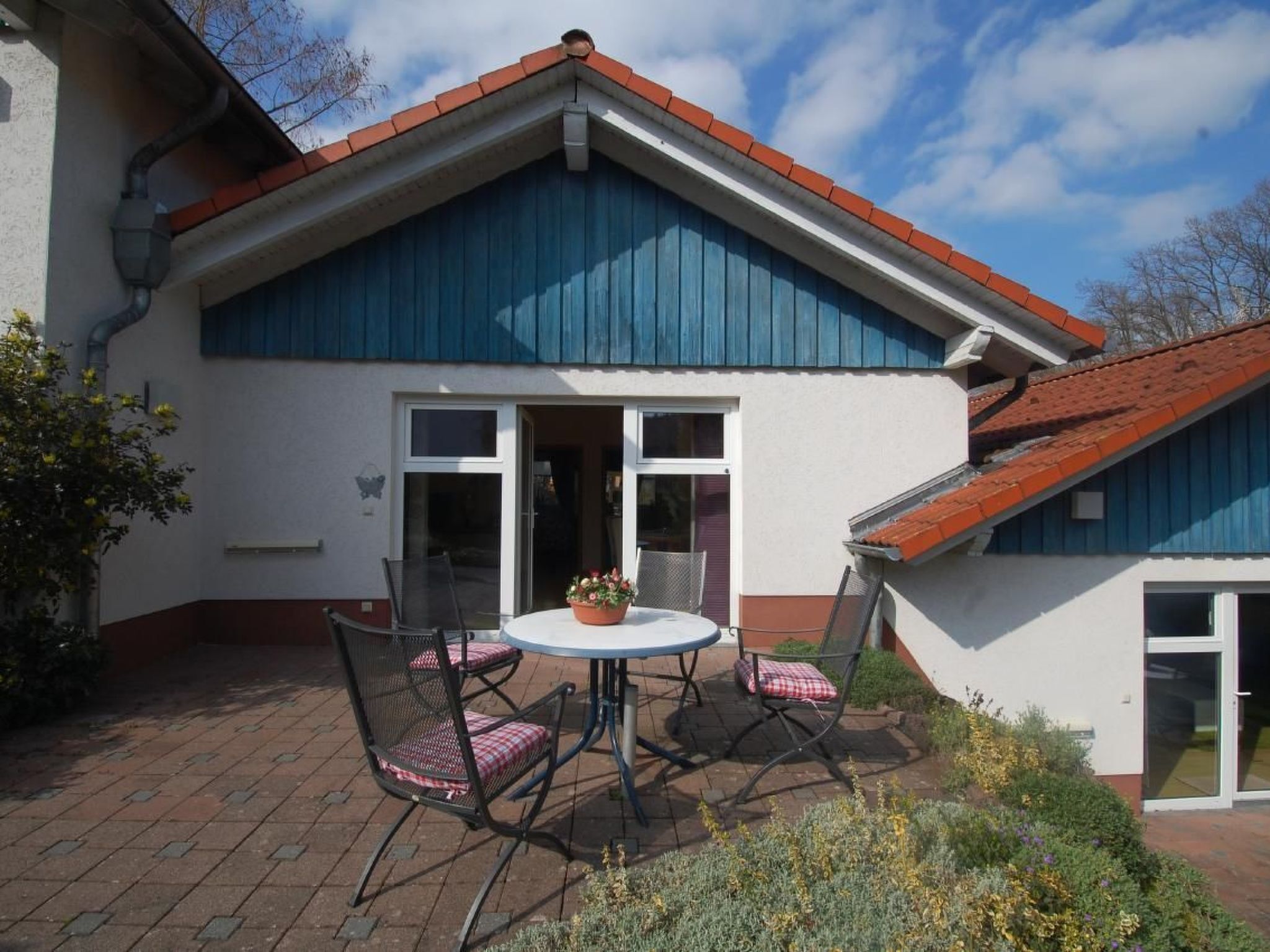 Ein Haus mit blauer Fassade, rotem Dach und einer Terrasse mit Tisch und Stühlen.
