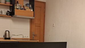 Un sofá color beige con patas de madera y un cojín amarillo en una habitación con piso de madera y una cocina al fondo.