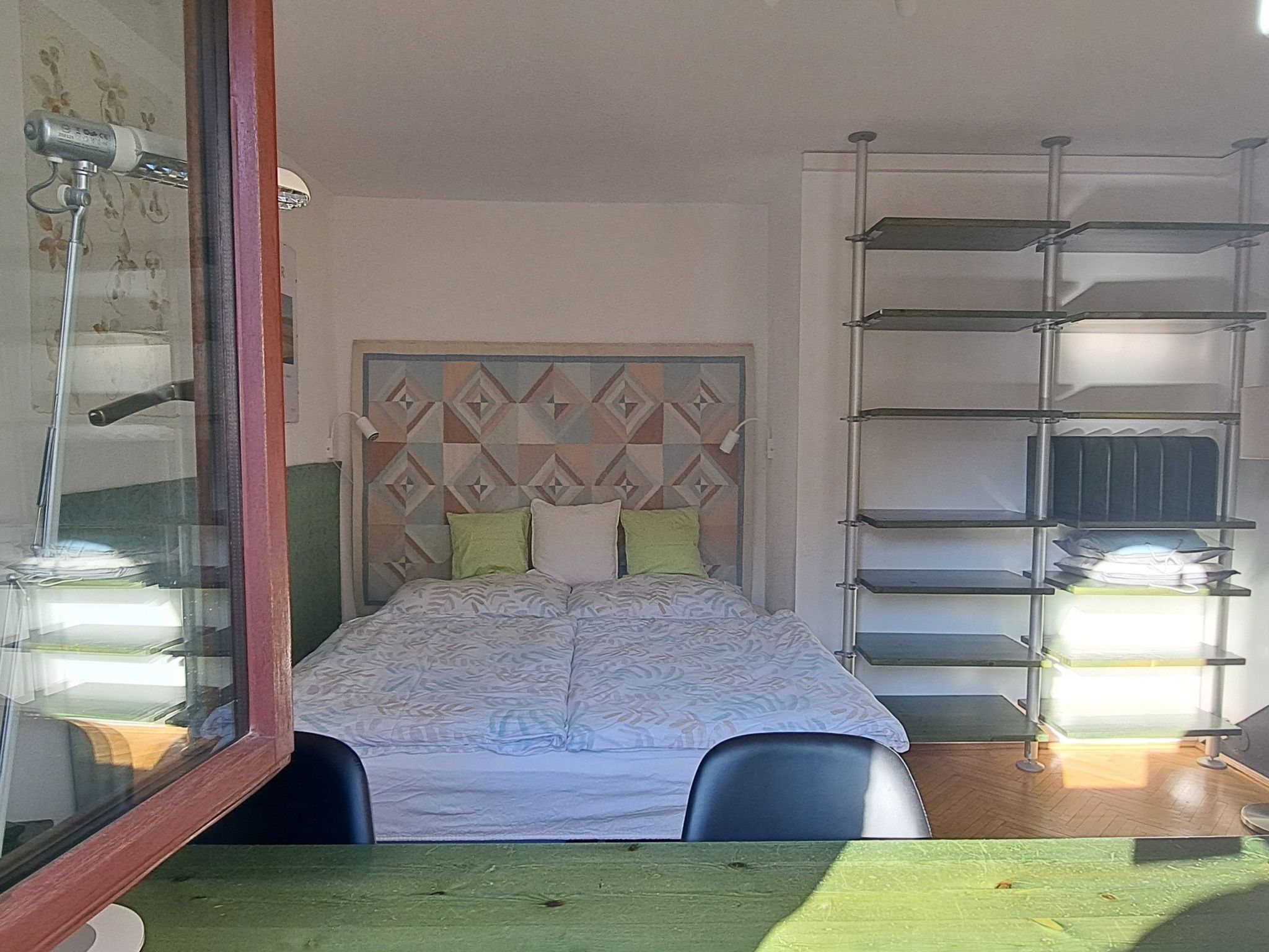 Ein Schlafzimmer mit einem Bett, einem Kopfteil mit geometrischen Mustern, einer Regaleinheit und einem Spiegel.