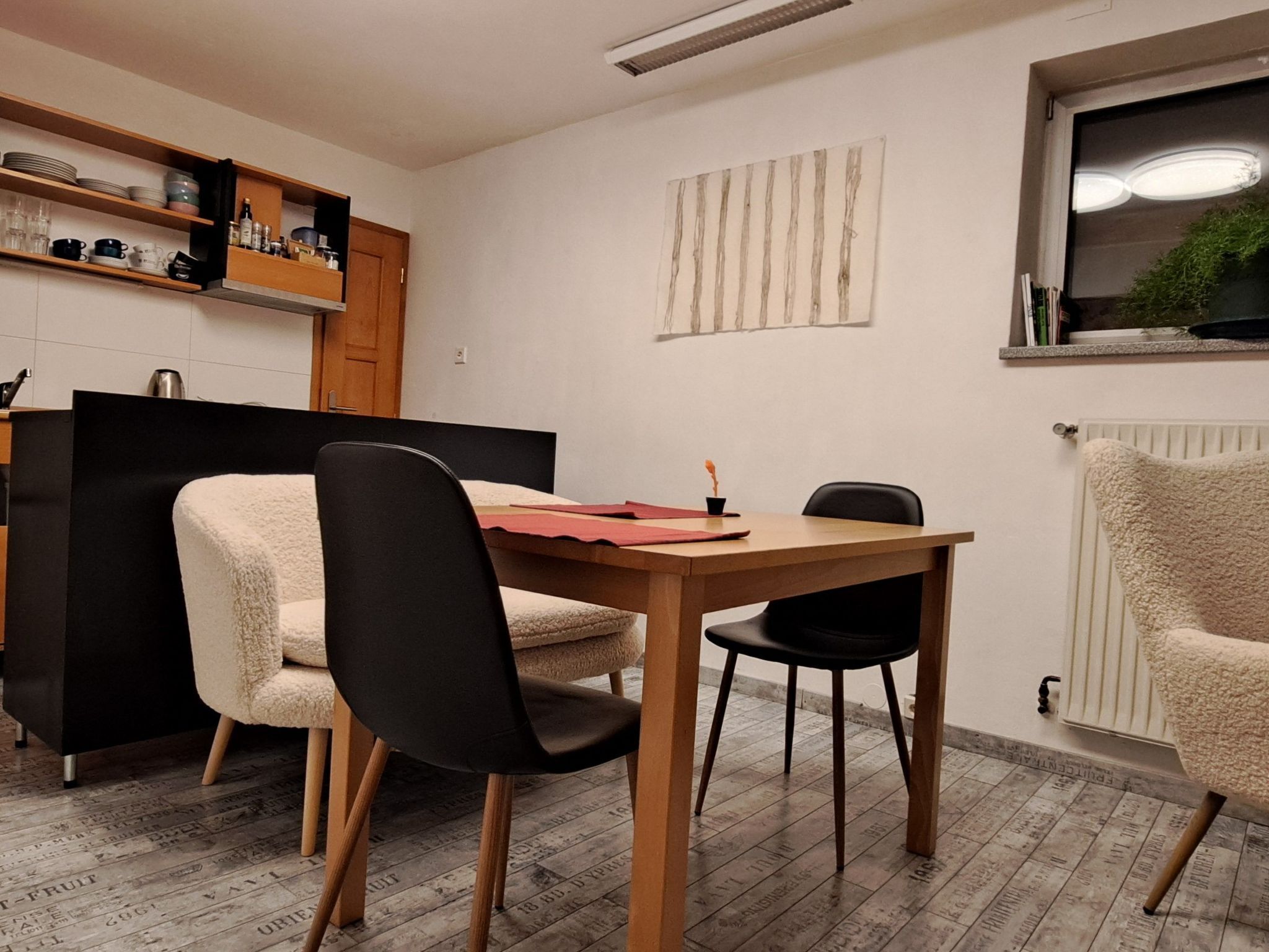 Cocina moderna con armarios de madera, una mesa de comedor y sillas. Se ve una ventana con una planta en el alféizar.