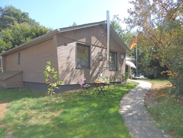 Een gelijkvloers huis met schuin dak, een klein voortuintje en een vlaggenmast.