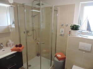 Een moderne badkamer met een glazen douche, een wastafel met spiegel en een raam met een plantje op de vensterbank.